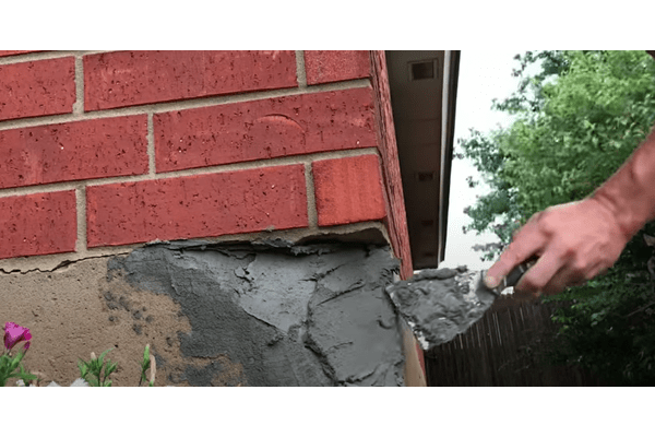 masonry contractor's hand using a metal tool to do parging services on the side of a brick building.